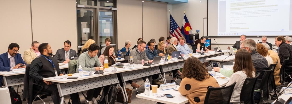 Several people sitting at a U-shaped conference table in a conference room.